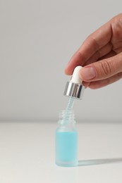 Woman with cosmetic serum at white table, closeup