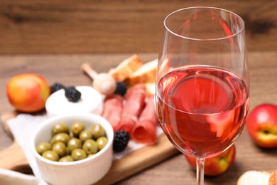 Glass of delicious rose wine and snacks on table, closeup