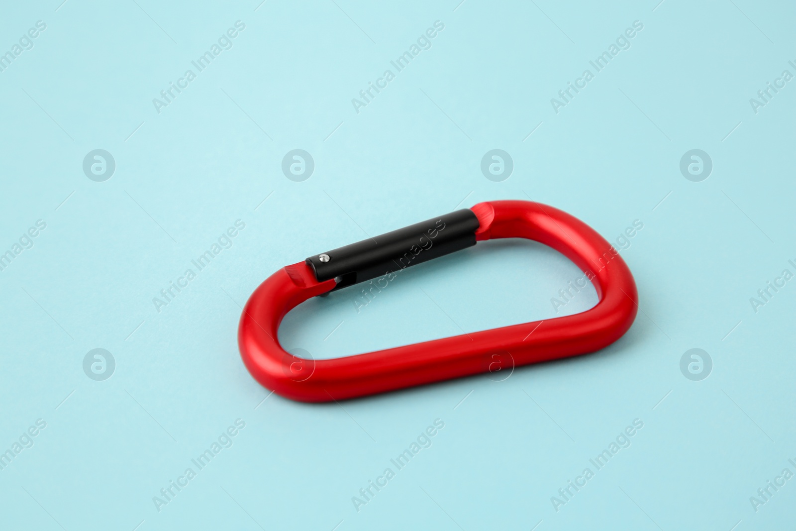 Photo of One red carabiner on light blue background, closeup