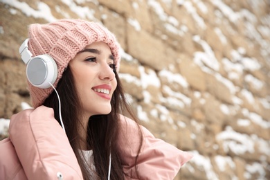 Photo of Young woman listening to music with headphones against stone wall. Space for text