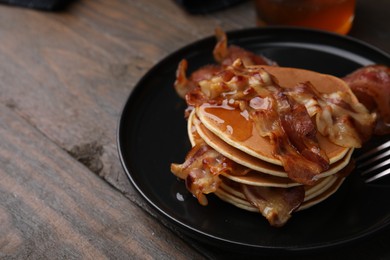 Photo of Delicious pancakes with fried bacon served on wooden table, closeup. Space for text