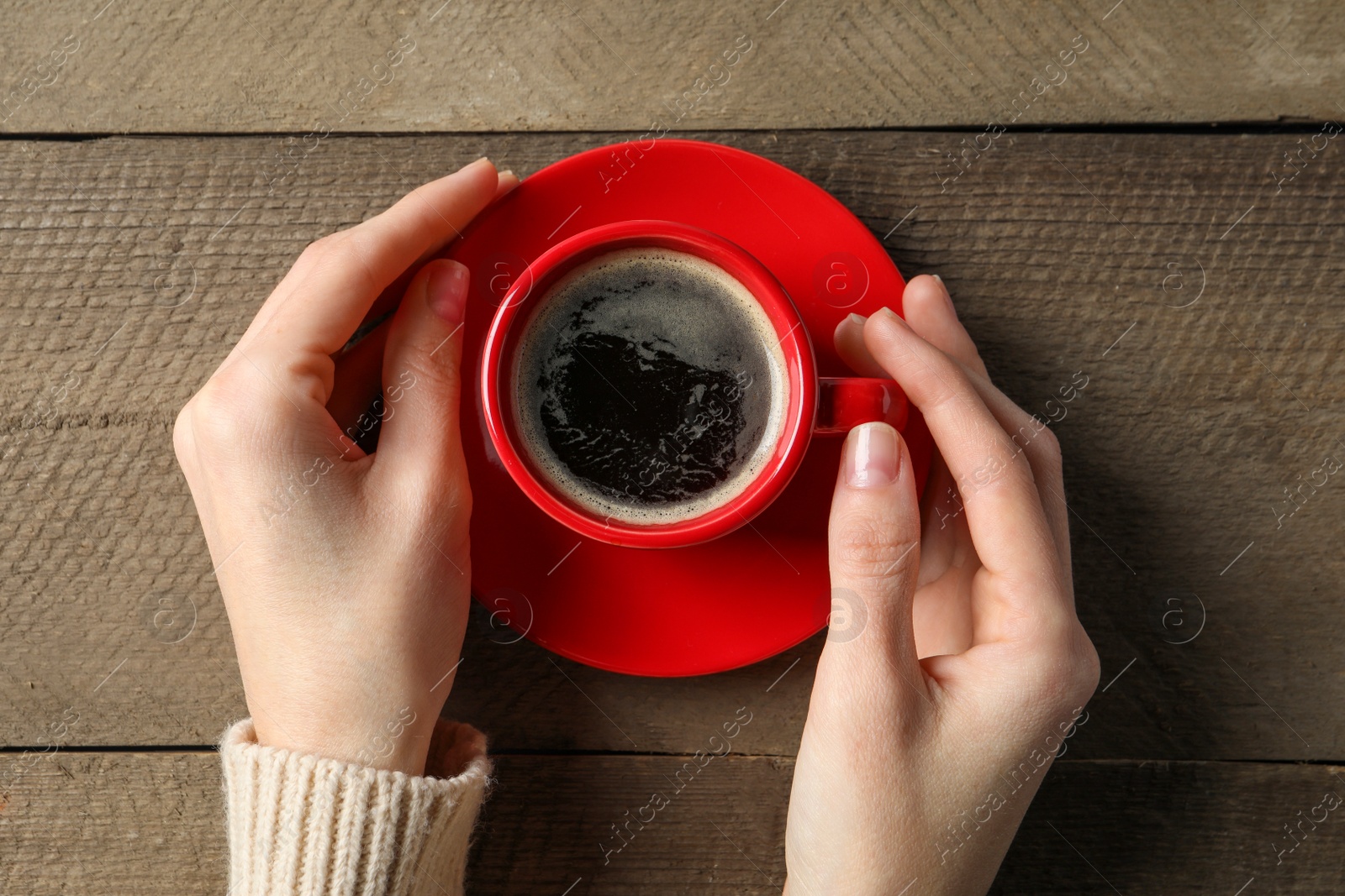 Photo of Woman holding cup of aromatic coffee at wooden table, top view