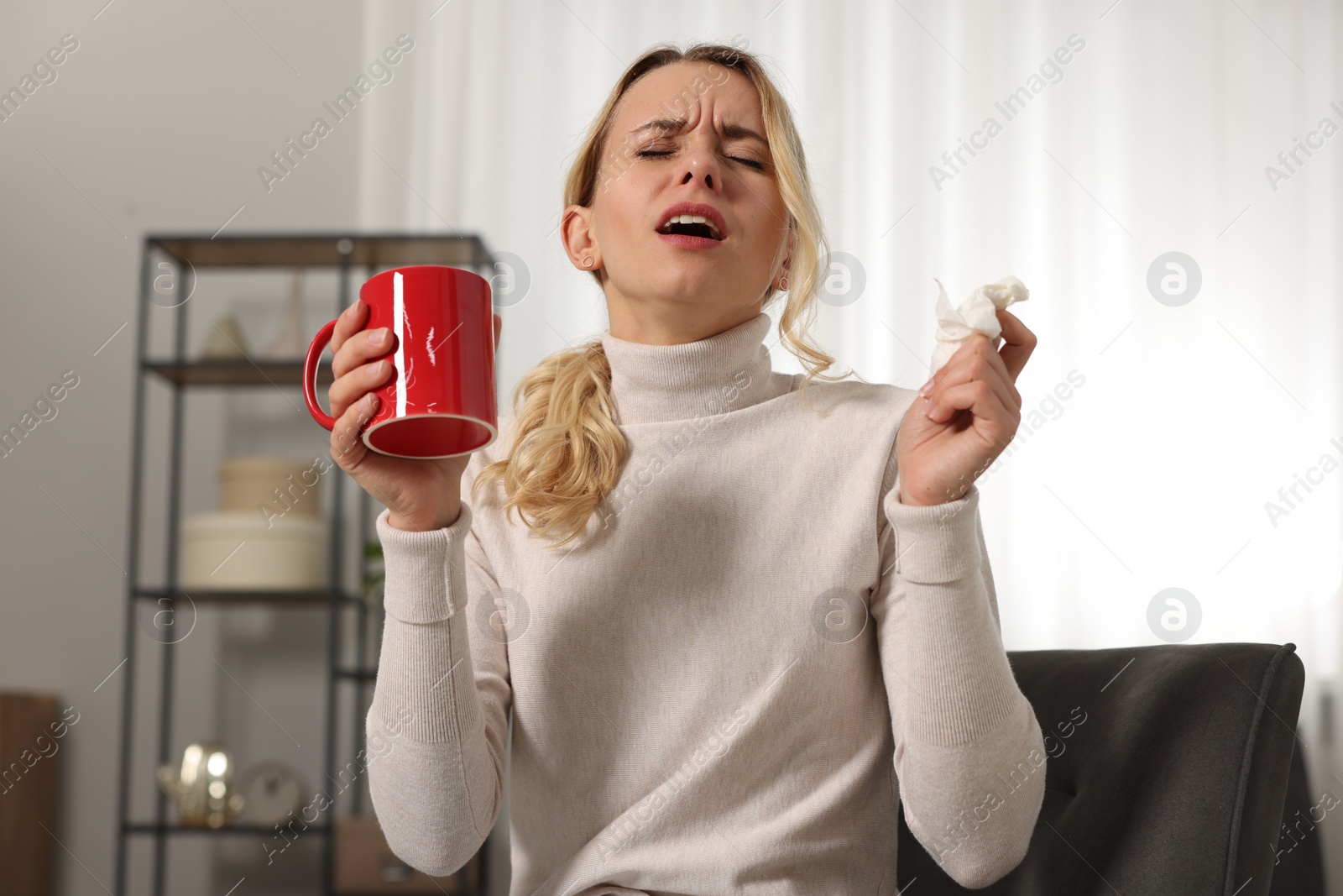 Photo of Sick woman with tissue and cup of drink sneezing at home. Cold symptoms