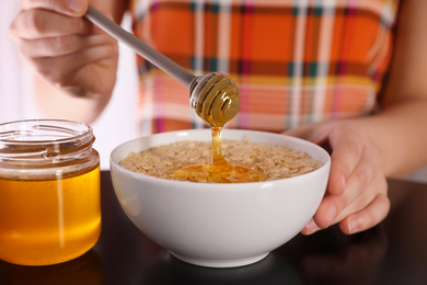 Photo of Woman adding honey to oatmeal at black table, closeup
