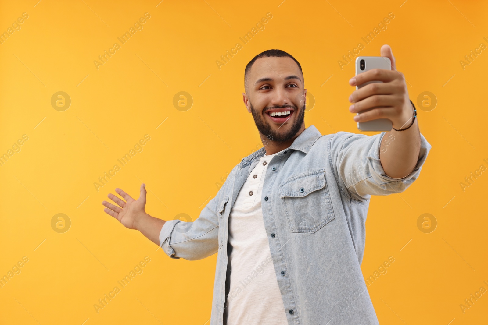 Photo of Smiling young man taking selfie with smartphone on yellow background