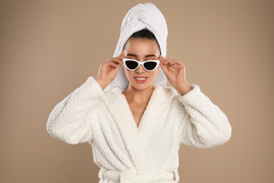 Young woman in bathrobe and sunglasses on brown background