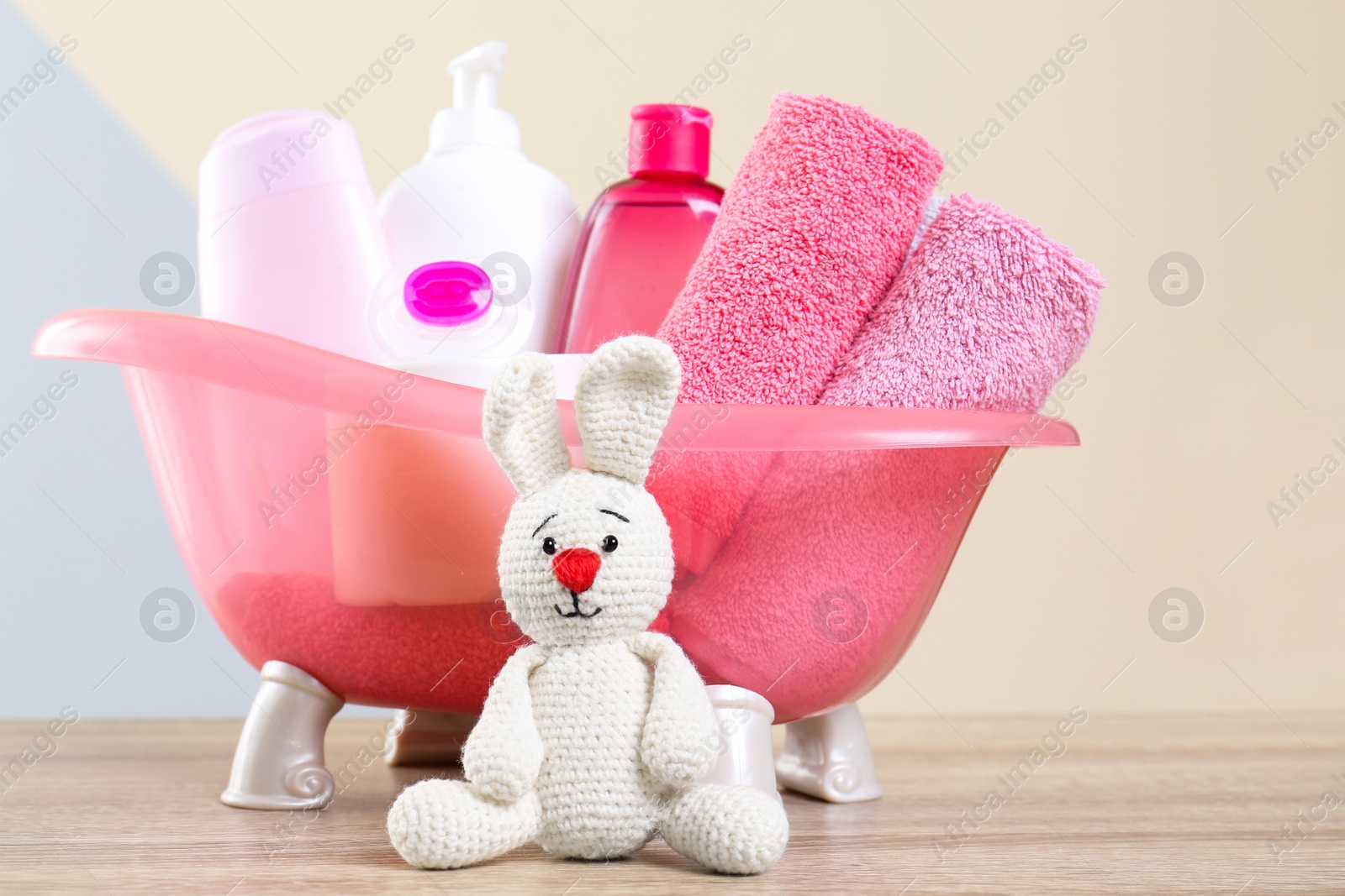 Photo of Baby cosmetic products, knitted rabbit and towels on table against color background