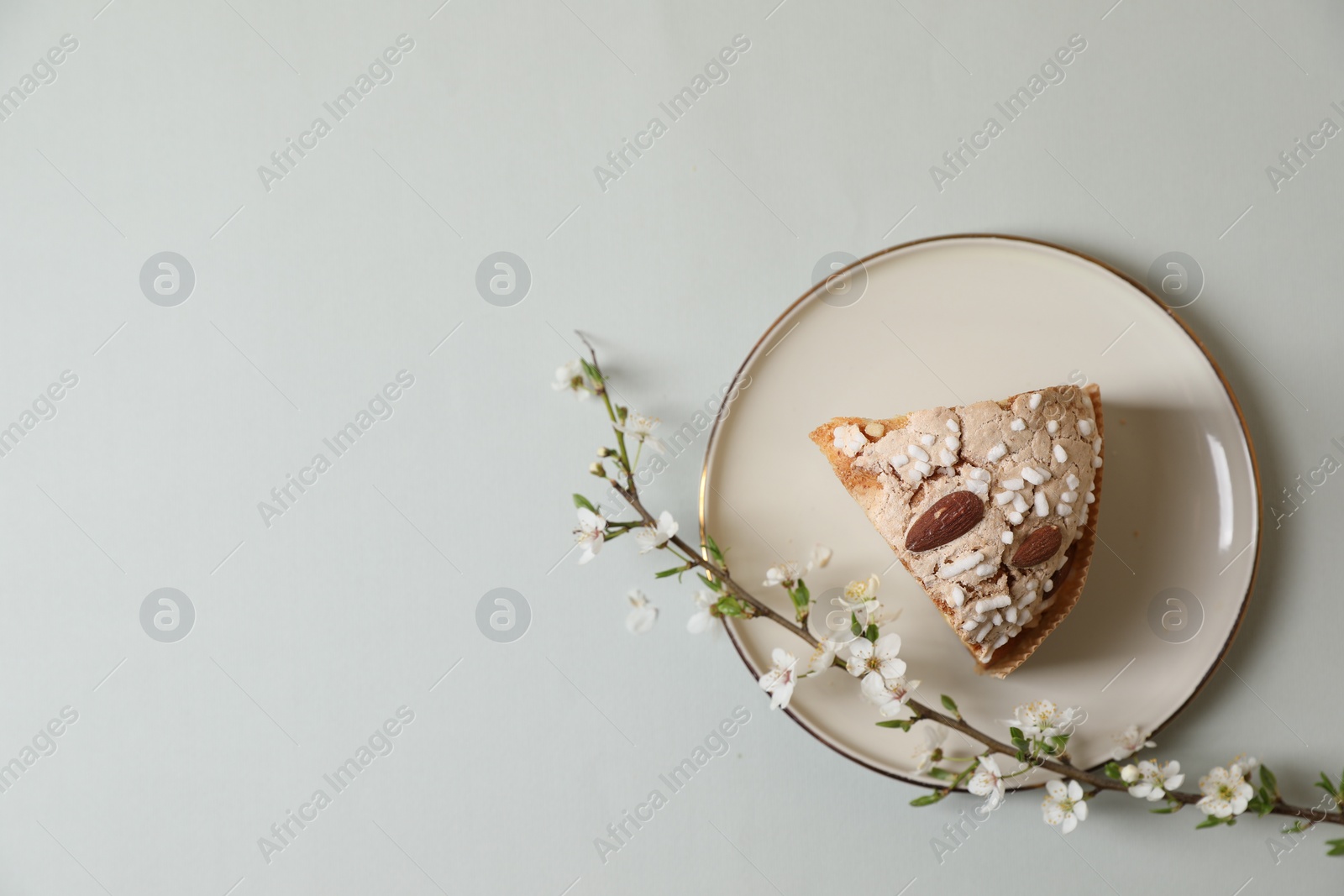 Photo of Plate with piece of delicious Italian Easter dove cake (traditional Colomba di Pasqua) and flowering branches on light grey table, top view. Space for text