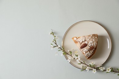 Plate with piece of delicious Italian Easter dove cake (traditional Colomba di Pasqua) and flowering branches on light grey table, top view. Space for text