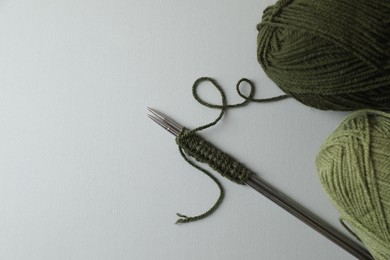 Soft green yarns, knitting and metal needles on light background, flat lay. Space for text