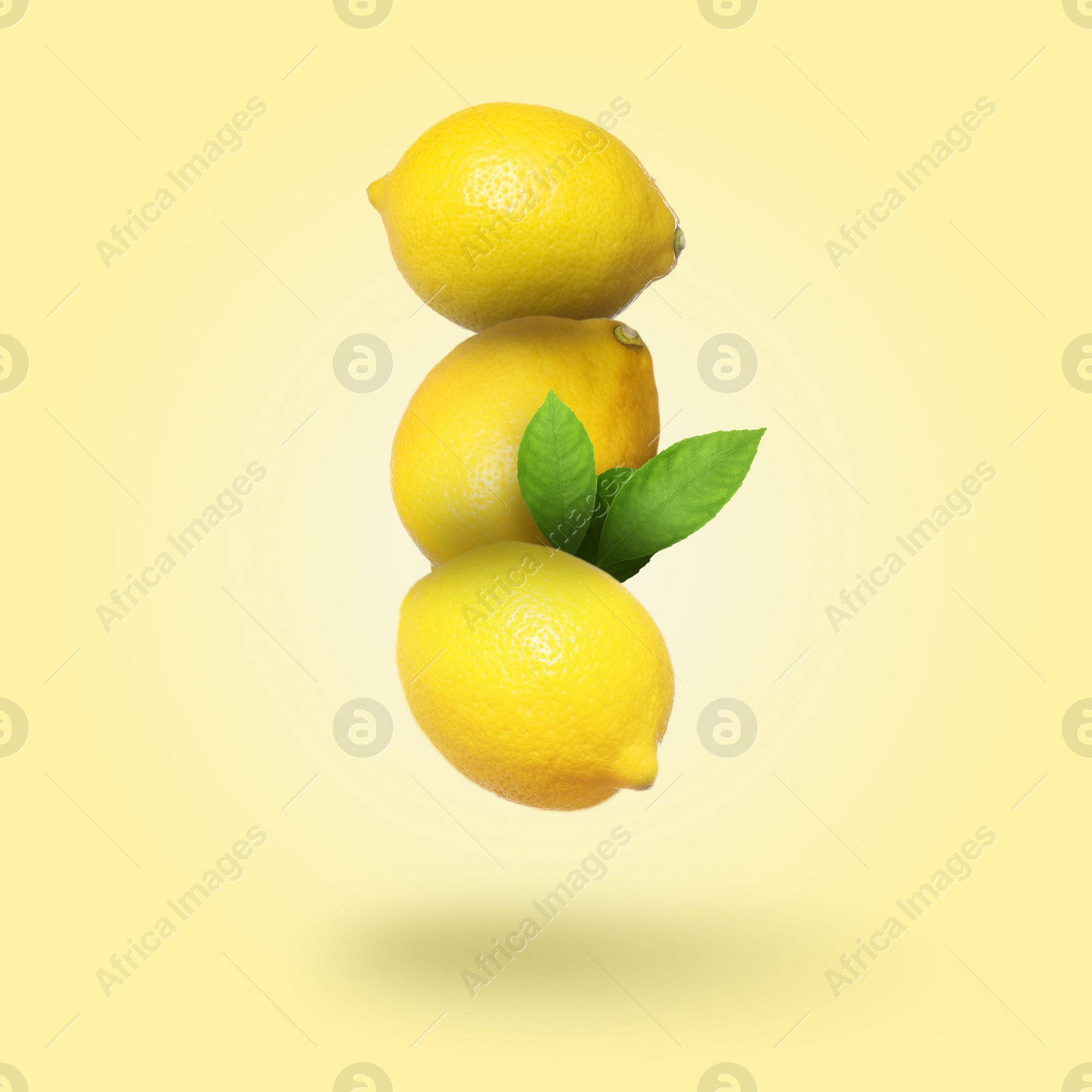 Image of Whole fresh lemons with green leaves falling on pale goldenrod background