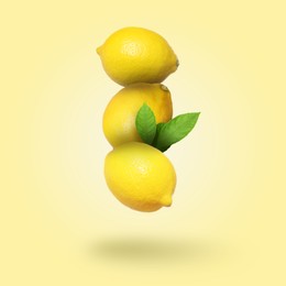 Whole fresh lemons with green leaves falling on pale goldenrod background