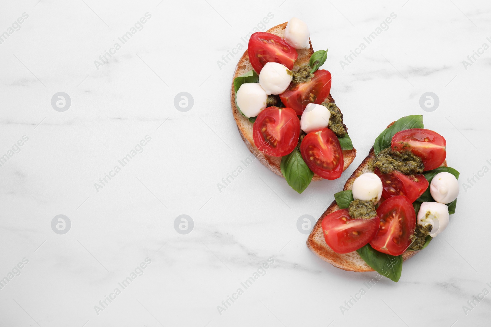 Photo of Delicious Caprese sandwiches with mozzarella, tomatoes, basil and pesto sauce on white marble table, flat lay. Space for text