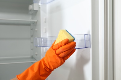 Photo of Worker in rubber gloves cleaning empty refrigerator, closeup