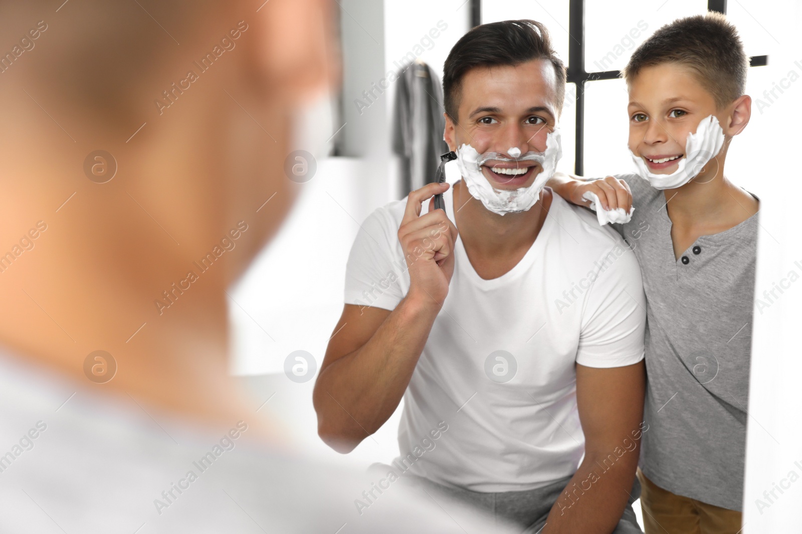 Photo of Dad showing his son how to shave near mirror in bathroom