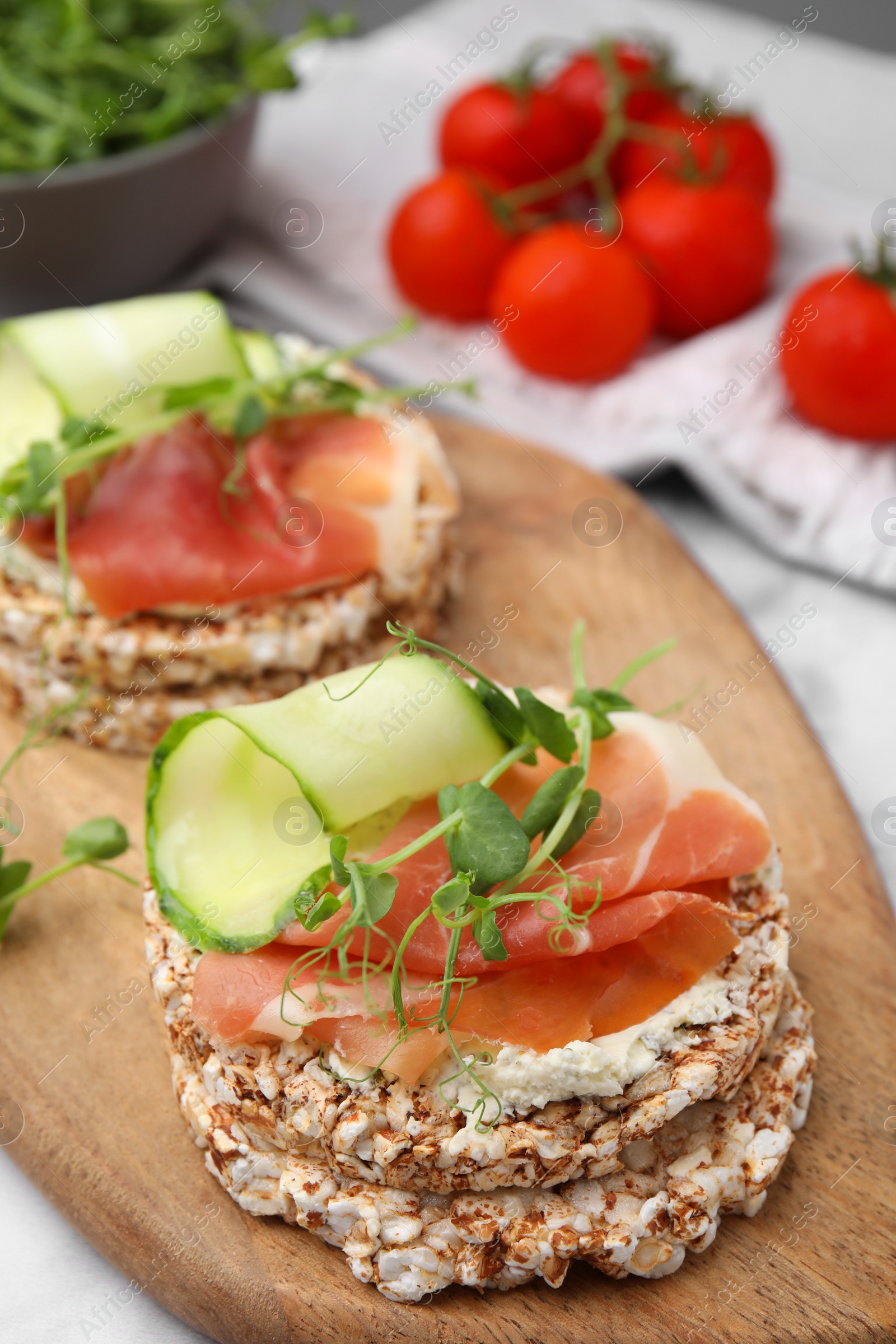 Photo of Crunchy buckwheat cakes with cream cheese, prosciutto and cucumber slices on wooden board, closeup