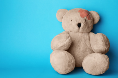 Photo of Toy teddy bear with sticking plasters on light blue background, space for text