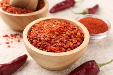 Photo of Chili pepper flakes and pods on light textured table, closeup