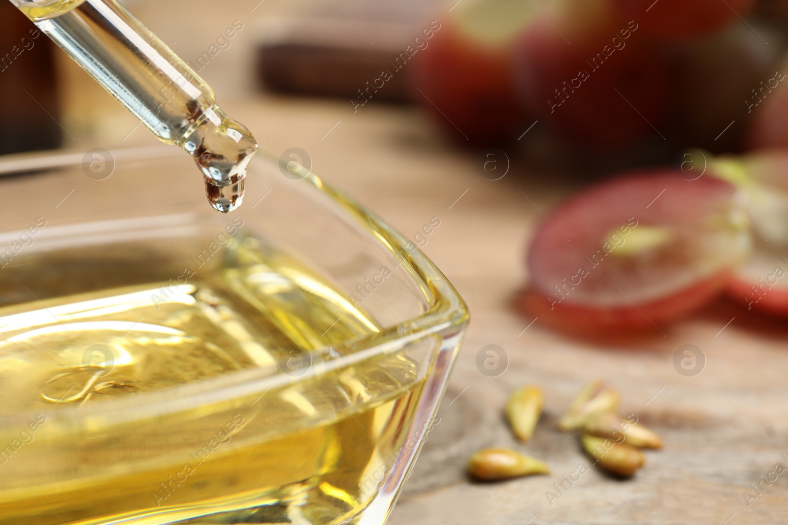 Photo of Dripping natural grape seed oil from pipette into bowl on wooden table, closeup. Organic cosmetic