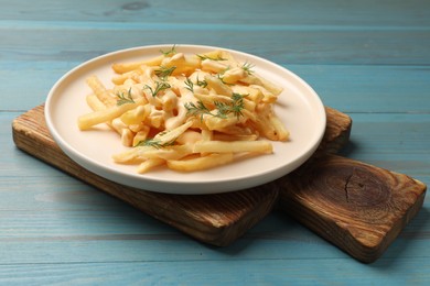 Photo of Delicious french fries with cheese sauce and dill on light blue wooden table