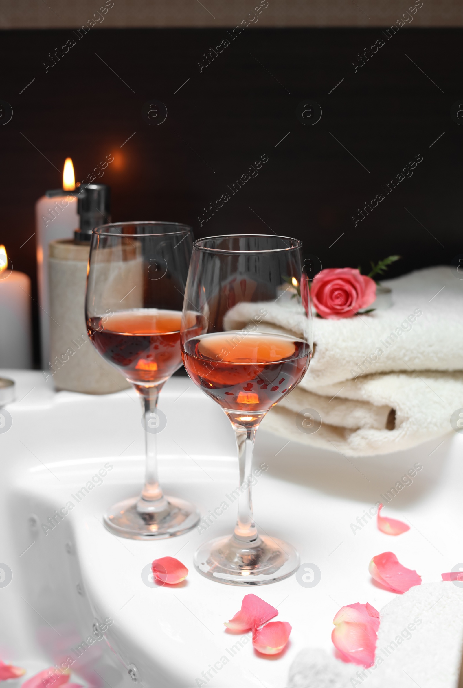 Photo of Wine in glasses, towels and rose on edge of bath indoors. Romantic atmosphere