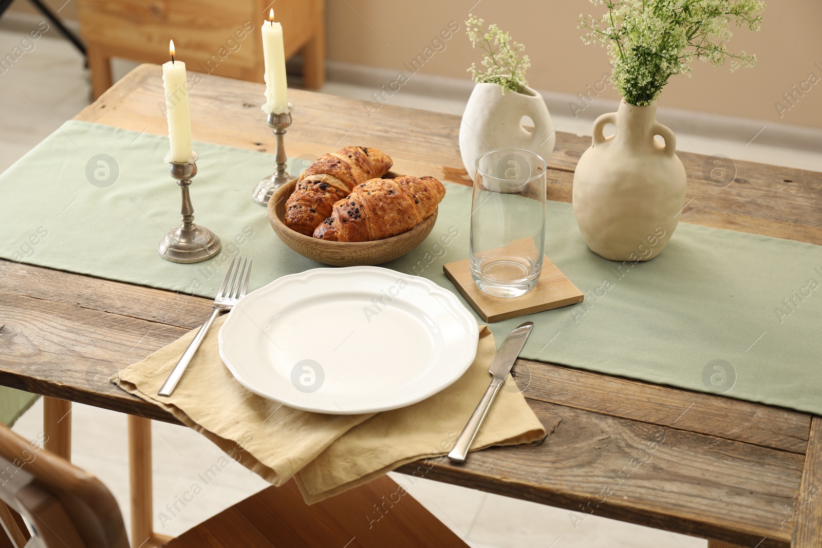 Photo of Clean tableware, candlesticks, flowers and fresh pastries on wooden table indoors