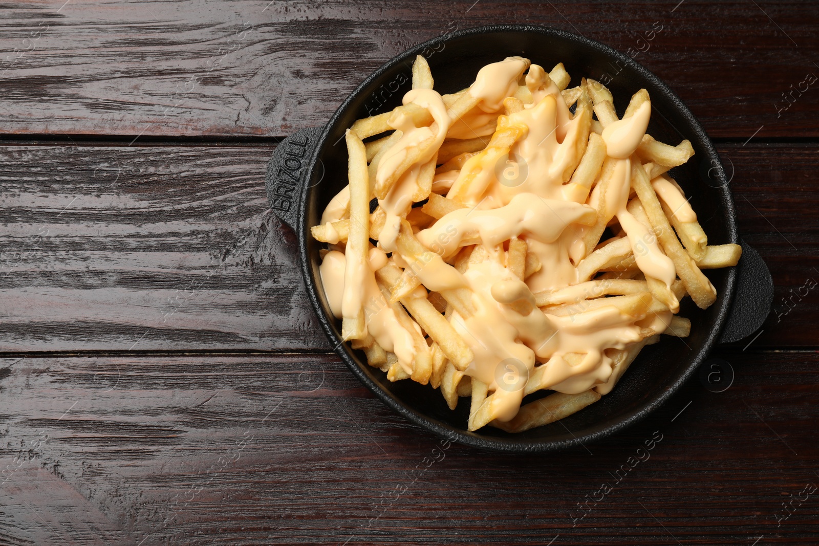 Photo of Delicious french fries with cheese sauce in bowl on wooden table, top view. Space for text