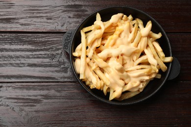 Photo of Delicious french fries with cheese sauce in bowl on wooden table, top view. Space for text