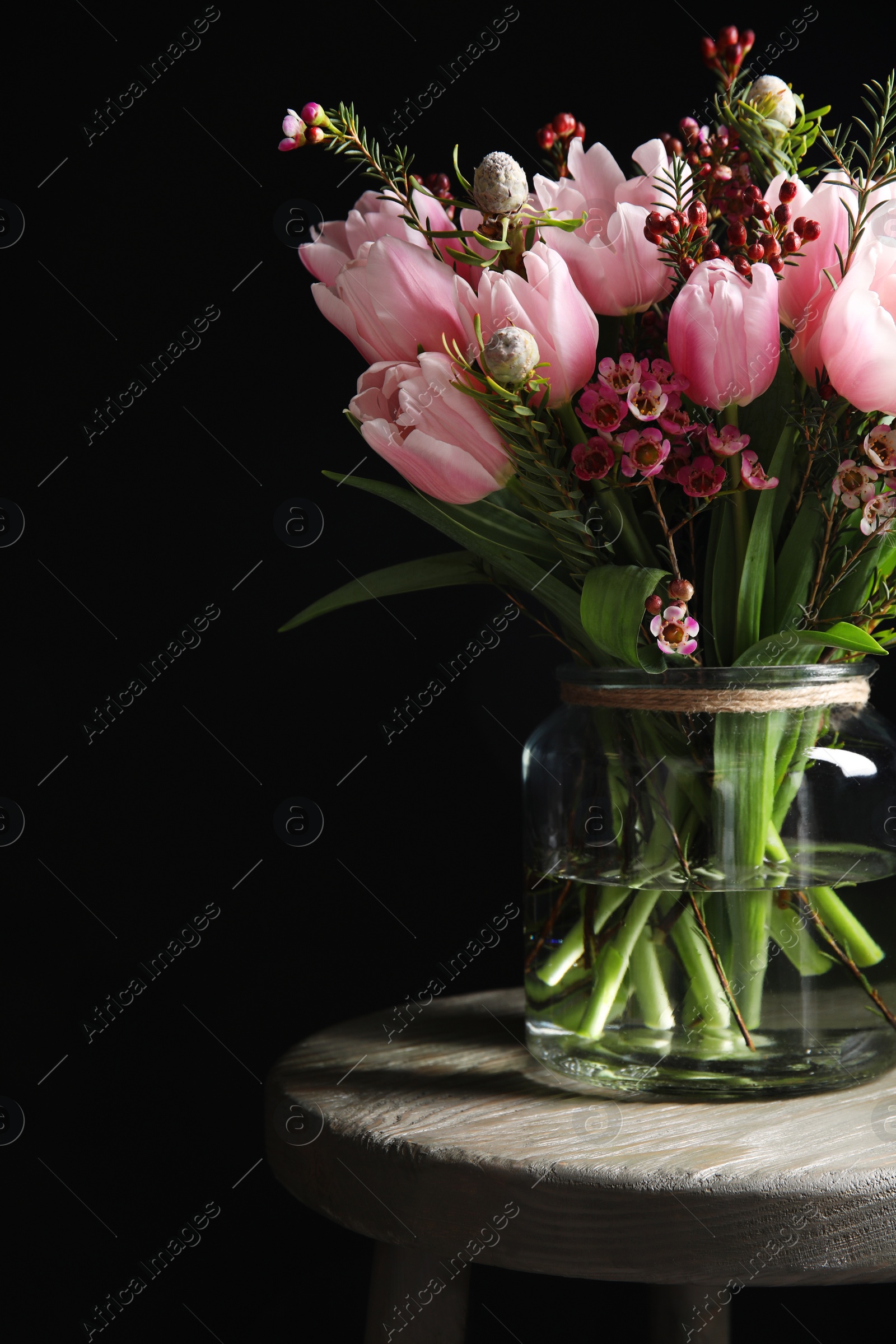 Photo of Beautiful bouquet with spring pink tulips on wooden table against black background