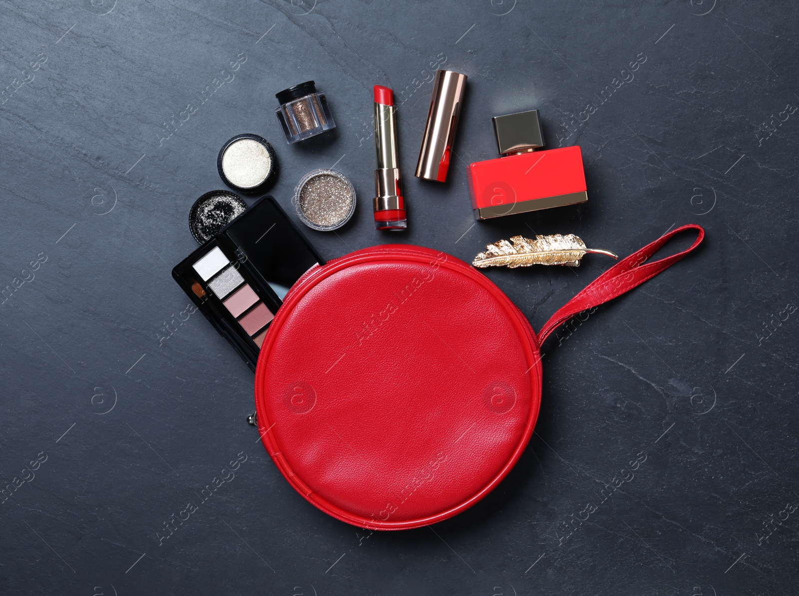 Photo of Cosmetic bag with makeup products on black slate background, flat lay