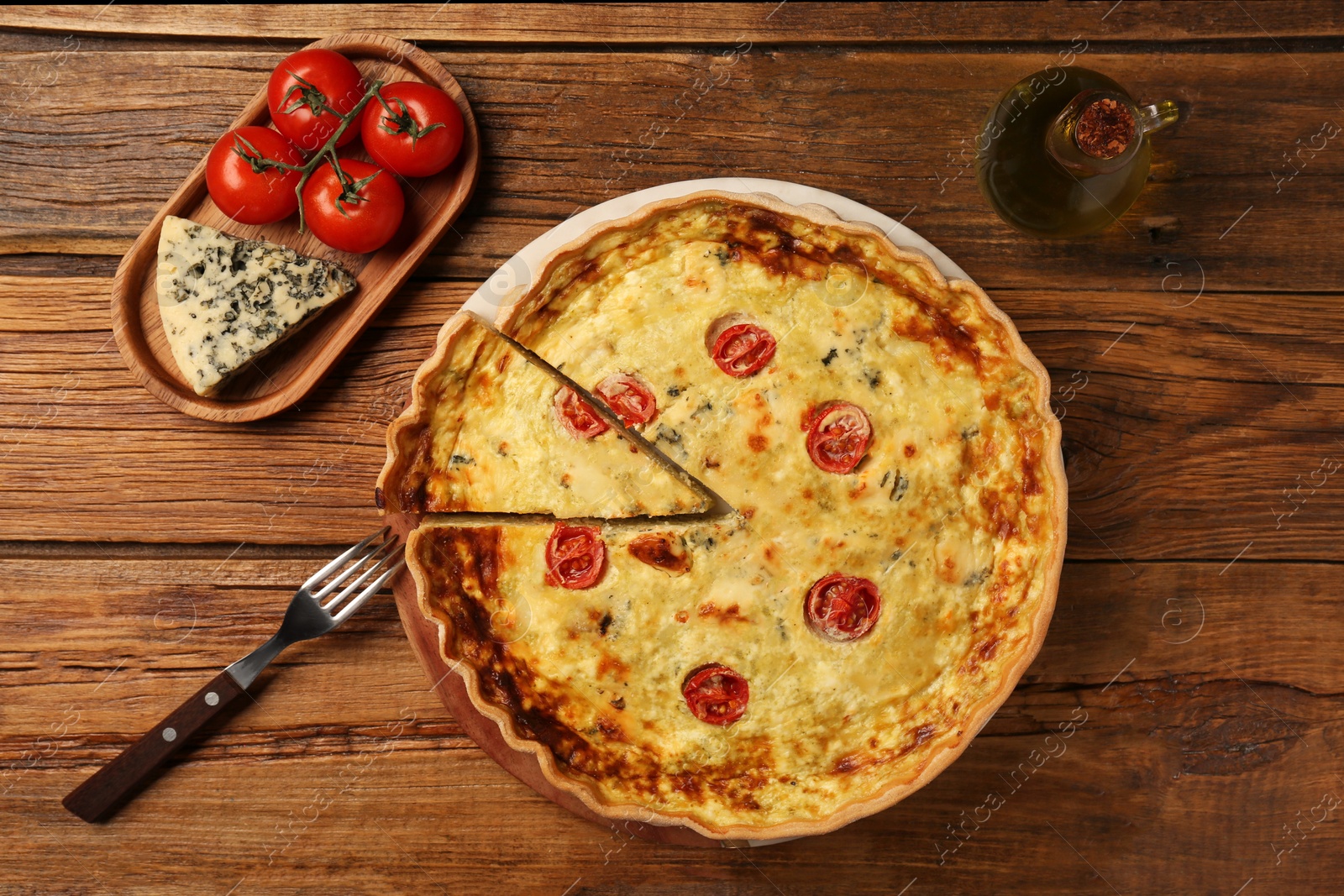 Photo of Delicious homemade cheese quiche, ingredients and fork on wooden table, flat lay