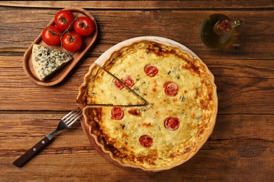 Photo of Delicious homemade cheese quiche, ingredients and fork on wooden table, flat lay