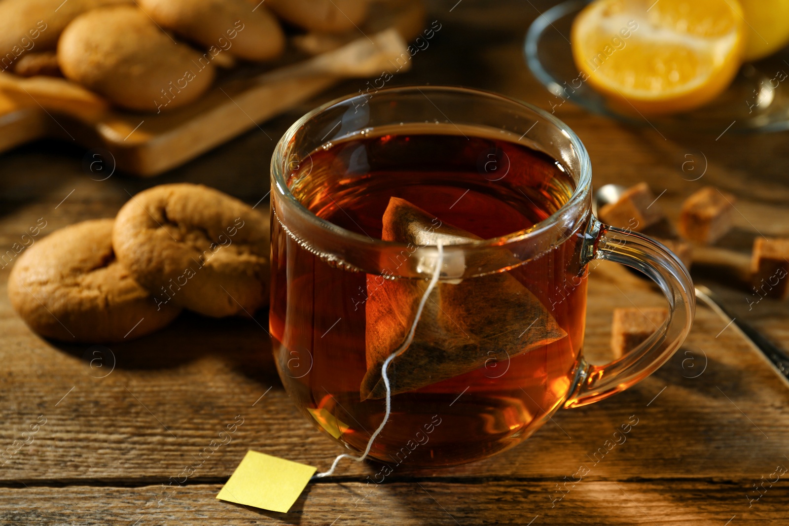 Photo of Tea bag in glass cup of hot water on wooden table