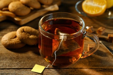 Photo of Tea bag in glass cup of hot water on wooden table