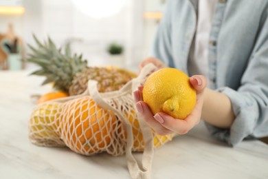Photo of Woman with string bag of fresh fruits and lemon at light table, closeup