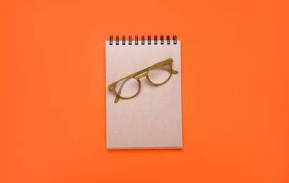 Photo of New office notebook and eyeglasses on orange background, top view