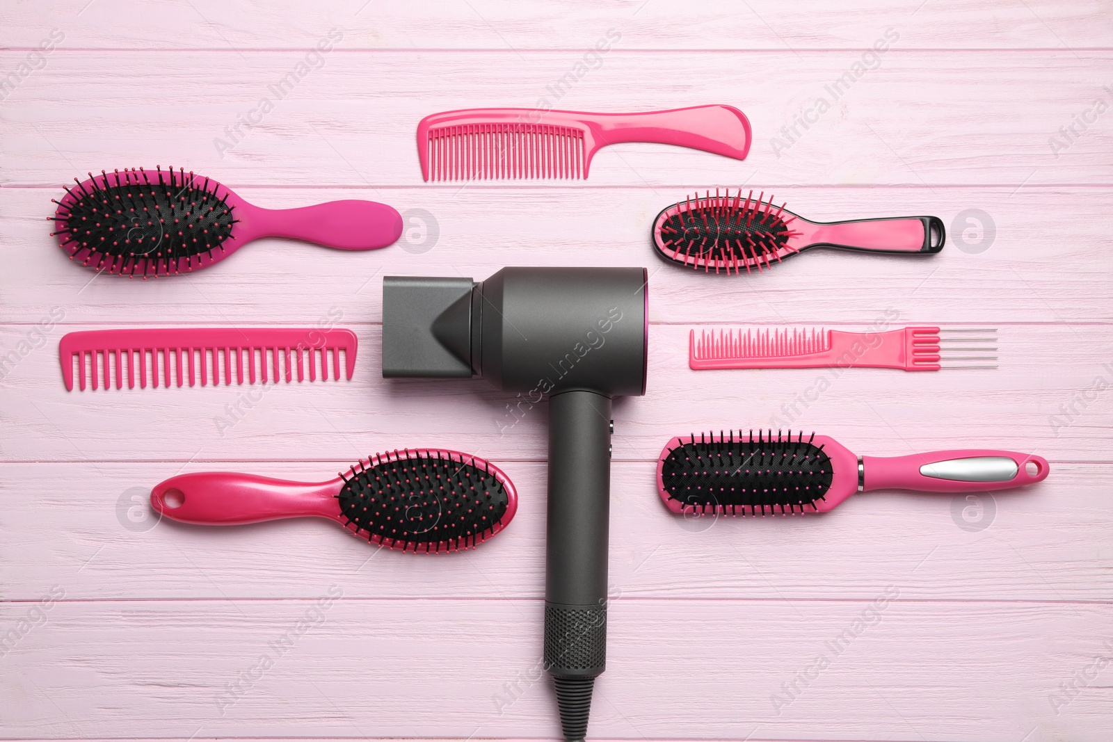 Photo of Hair dryer and different brushes on pink wooden table, flat lay. Professional hairdresser tool