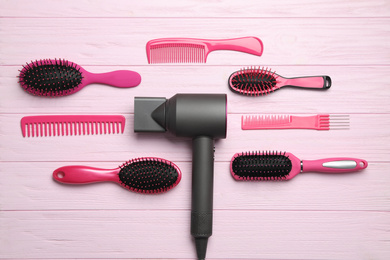 Hair dryer and different brushes on pink wooden table, flat lay. Professional hairdresser tool