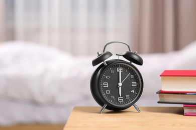 Photo of Black alarm clock and books on wooden table indoors. Space for text