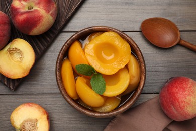 Photo of Canned peach halves in bowl on wooden table, flat lay