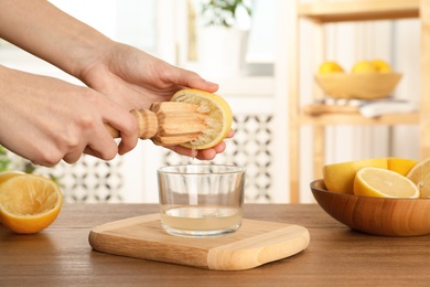 Photo of Woman squeezing lemon juice with wooden reamer into glass bowl at table