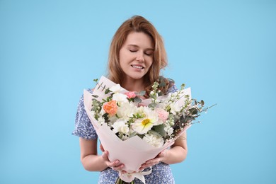 Happy woman with bouquet of beautiful flowers on light blue background