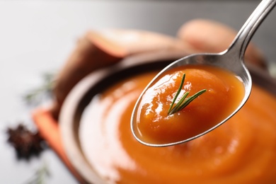 Spoon with tasty sweet potato soup over table, closeup. Space for text