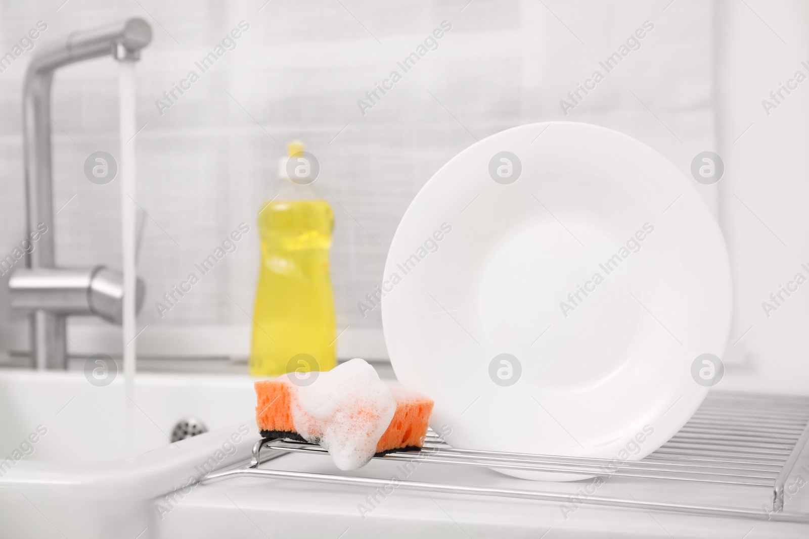 Photo of Drying rack with clean plate and soapy sponge in stylish kitchen