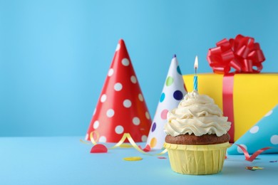 Photo of Delicious birthday cupcake with candle on light blue background, space for text