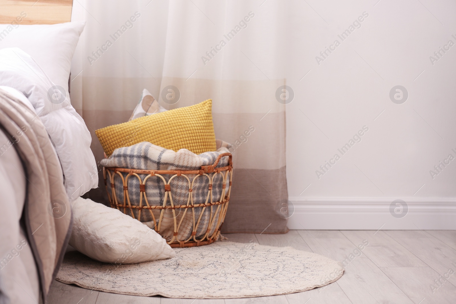 Photo of Basket with blanket and pillows near bed indoors