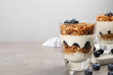 Glasses of yogurt with granola and blueberries on grey table, closeup. Space for text