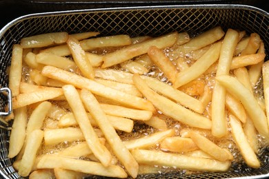 Cooking delicious french fries in hot oil, closeup