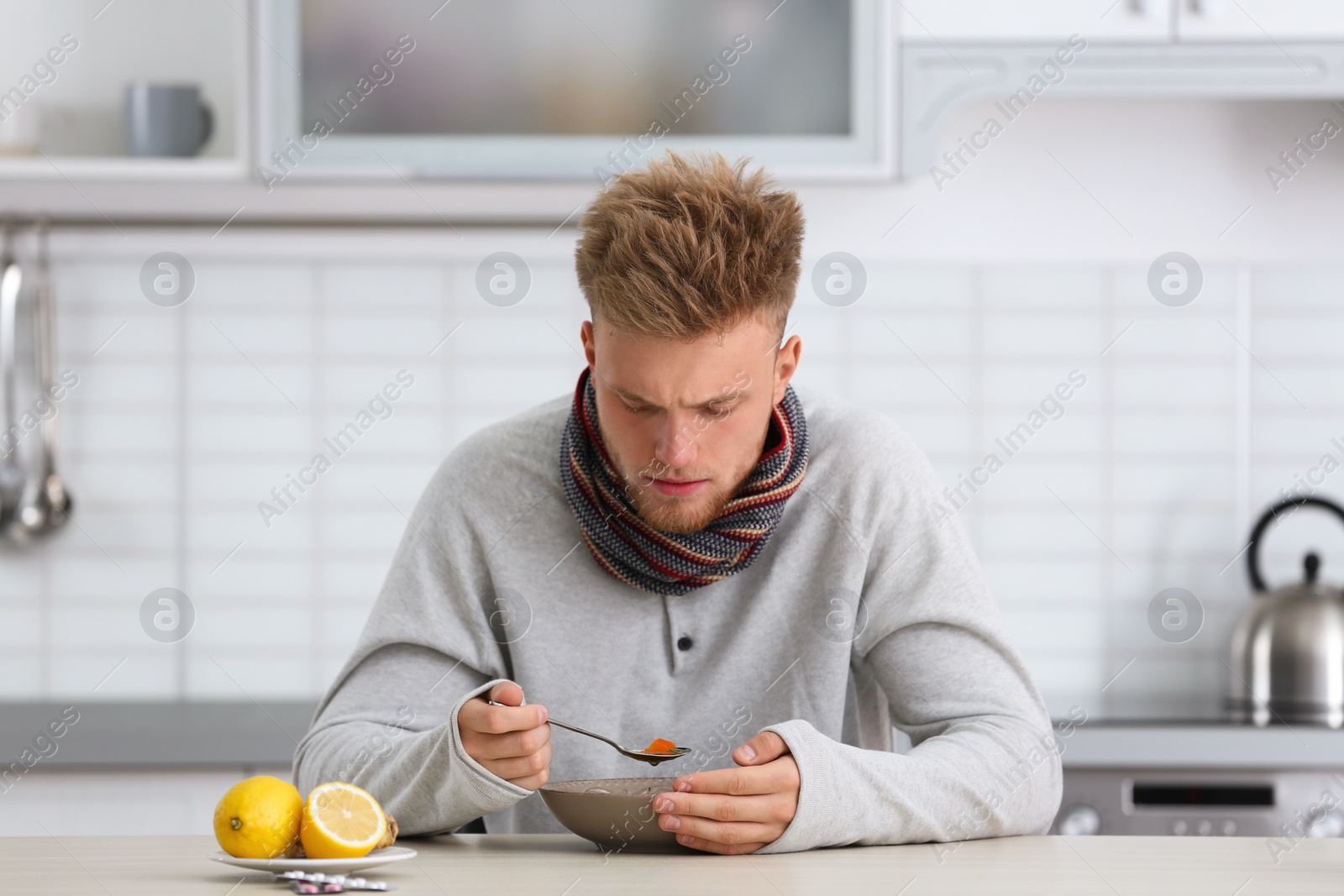 Photo of Sick young man eating soup to cure flu at table in kitchen
