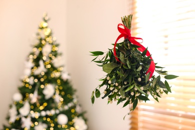 Mistletoe bunch with red bow hanging in room decorated for Christmas, space for text